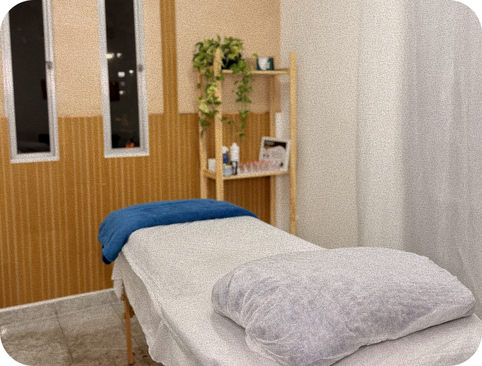 Sala de atendimento com maca preparada, toalha azul e prateleira com plantas